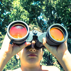 Low angle view of boy holding binoculars against trees during sunny day