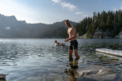 Shirtless mature man standing in lake against sky during sunny day