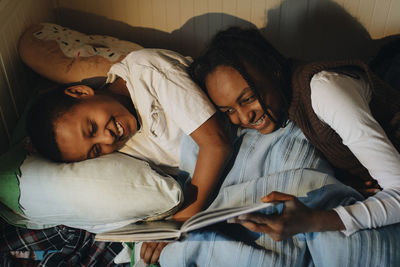 Happy siblings reading story book while lying on bed at home