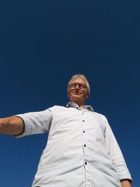 Low angle view of smiling senior man standing against clear blue sky during sunny day