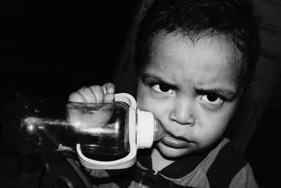 Close-up portrait of boy with milk bottle against black background