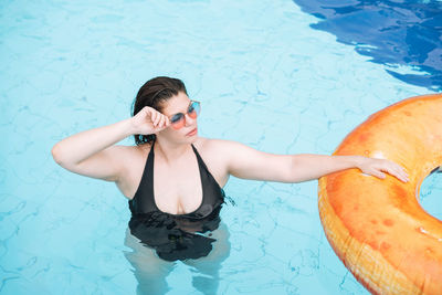 Happy young woman plus size body positive in inflatable doughnut circle swimming in the pool