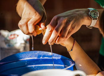 Cropped hand of parent with child breaking egg in container