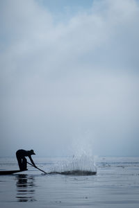 Silhouette man in boat on river against sky