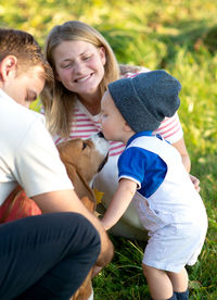 Baby boy playing with dog while standing by parents in park