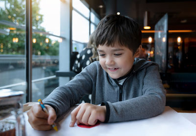 Boy drawing on paper while sitting in cafe