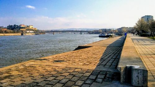 Footpath by river in city against sky