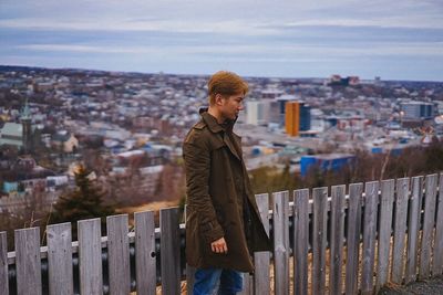 Man standing by fence against cityscape