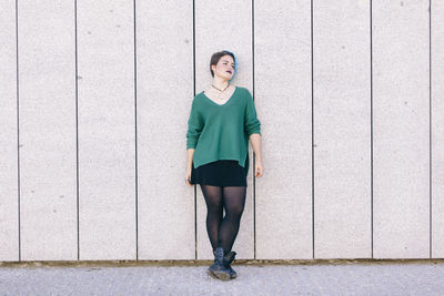 Portrait of a smiling young woman standing against wall