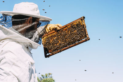 Beekeeper in workwear working against sky