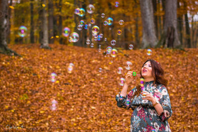 Mid adult woman blowing bubbles in forest during autumn