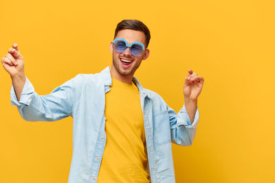 Portrait of young woman wearing sunglasses while standing against yellow wall