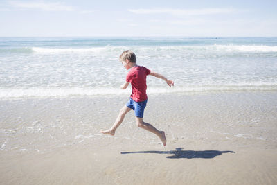 Full length side view of boy running at beach on sunny day