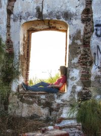 Rear view of woman sitting on window of old building