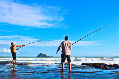 Men fishing on sea shore against sky