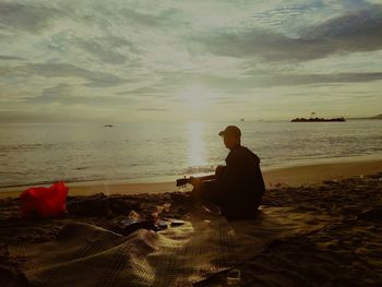 Woman sitting on shore at beach against sky