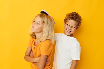 Smiling boy combing hair of sister against yellow background