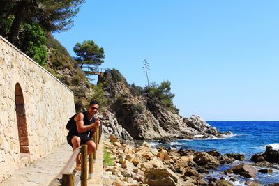 People sitting on rock by sea against clear sky