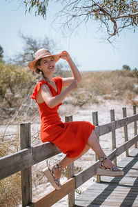 Full length portrait of smiling young woman sitting on railing