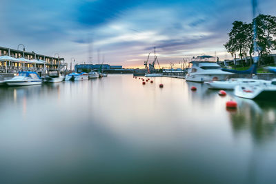 Sailboats moored at harbor in city against cloudy sky