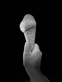 Close-up of hand holding ice cream against black background