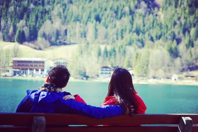 Rear view of couple sitting against lake on bench