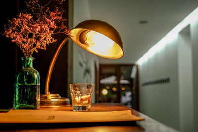 Illuminated electric lamp by glass on table at restaurant