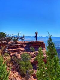 Woman practicing yoga on mountain against clear blue sky