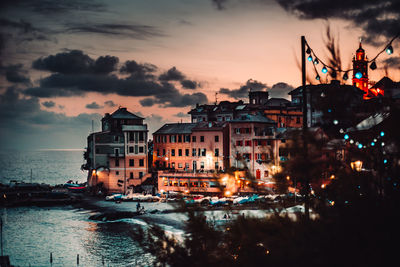 Buildings by sea against sky at sunset