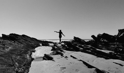 Carefree woman standing on rocks in snow against clear sky