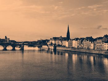 Bridge over river by buildings against sky during sunset