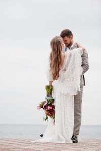 Bride and bridegroom standing on pier in sea during wedding ceremony