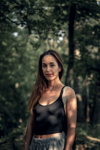 Portrait of young woman standing against trees