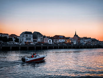 People in sea against buildings in city at sunset