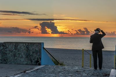 Rear view of person photographing sea against sky during sunset