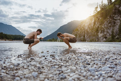 People on lake by mountains against sky