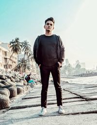 Full length portrait of young man standing against sky