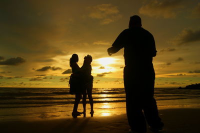 Silhouette family standing at beach against orange sky