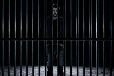 Portrait of man standing by metal grate in darkroom