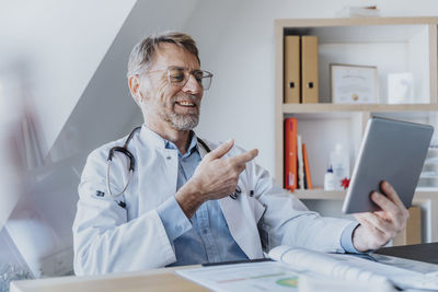 Smiling doctor talking on video call over digital tablet while sitting at clinic