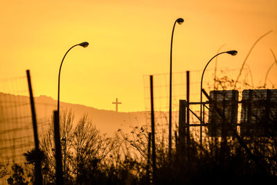 Silhouette plants and street lights against sky during sunset