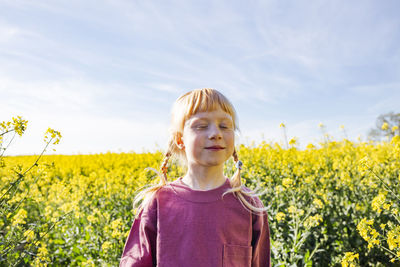 Smiling redheaded girl with eyes closed standing on rapeseed field