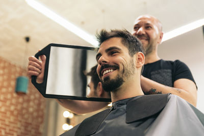 Low angle view of barber cutting man hair in salon