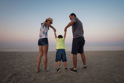 Rear view of cheerful family at beach during sunset