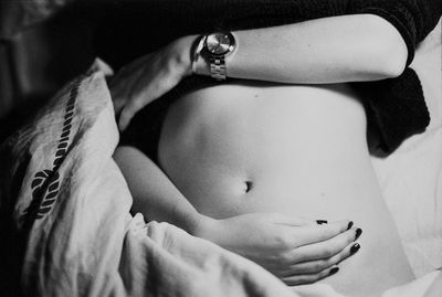 Midsection of pregnant woman with hands on stomach lying on bed at home