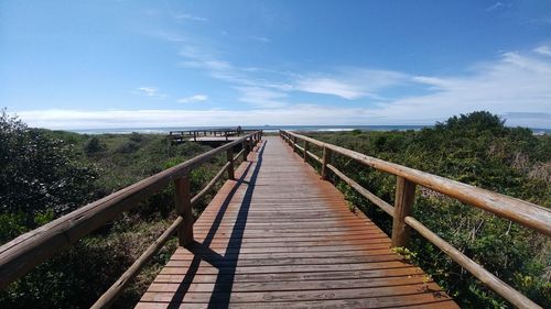Wooden footbridge on boardwalk against sky