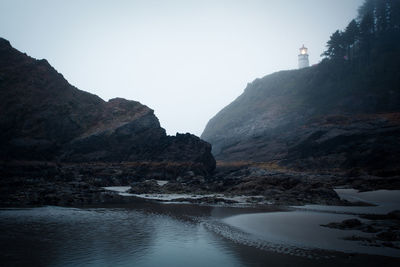Lighthouse on cliff by sea against sky