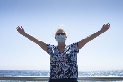 Smiling senior woman wearing mask standing by sea against sky
