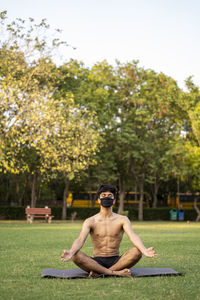 Full length of shirtless man sitting on tree