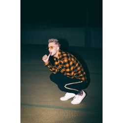 Full length of young man licking thumb while crouching on road